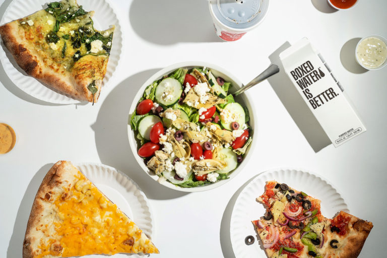Birdseye view of bowl of salad and slices of pizza on white table
