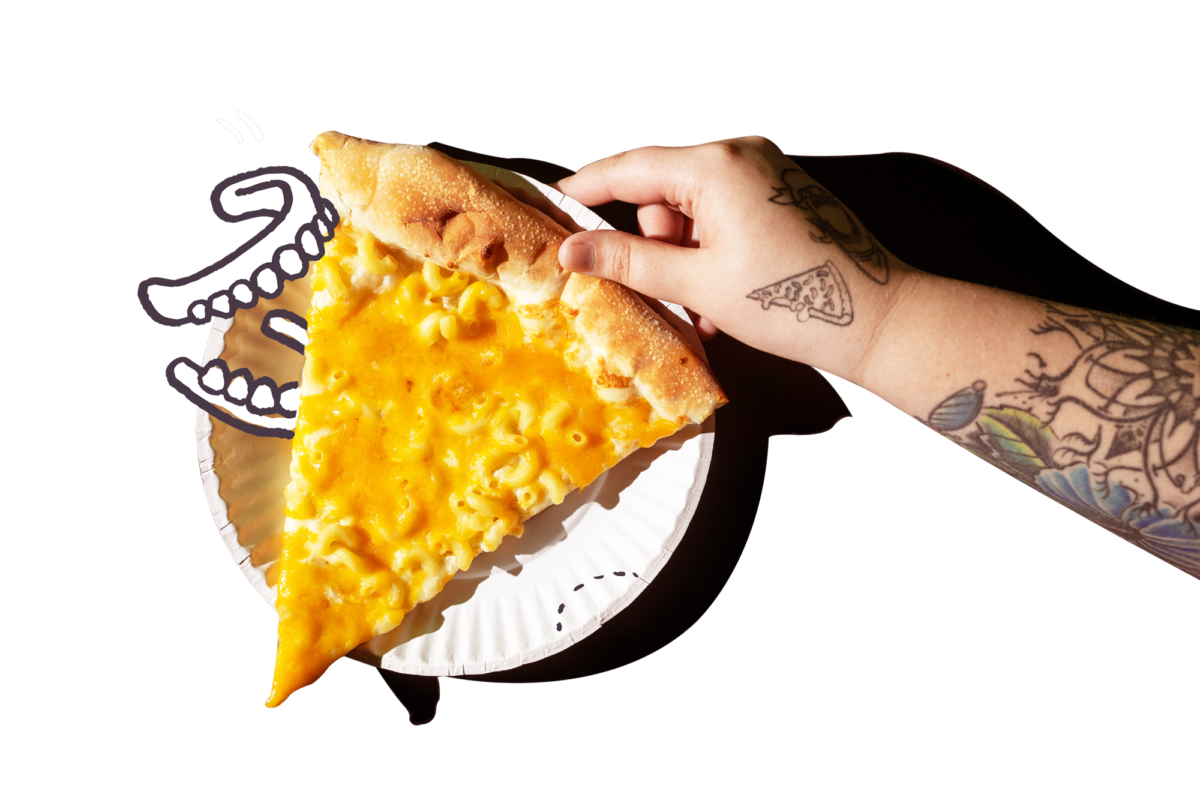 Hand holding slice of mac and cheese pizza on paper plate